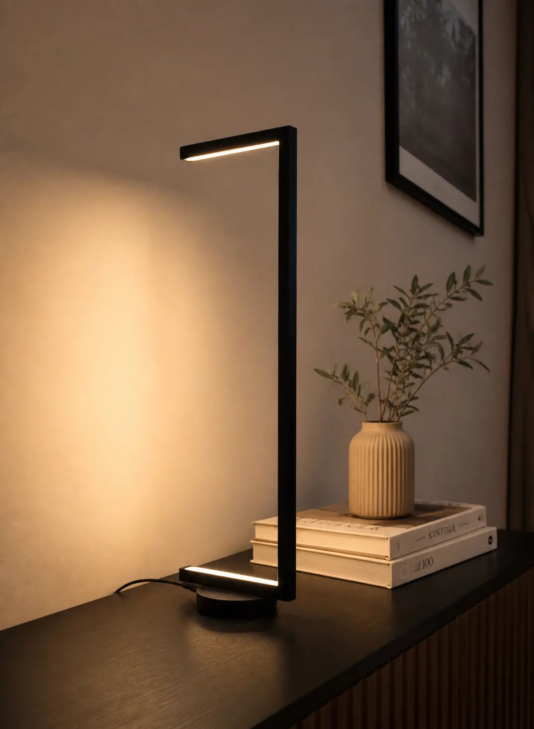 Tratto Table Lamp by Tommaso Cristofaro, a minimalist black sculptural lamp with warm indirect light reflected on the wall.