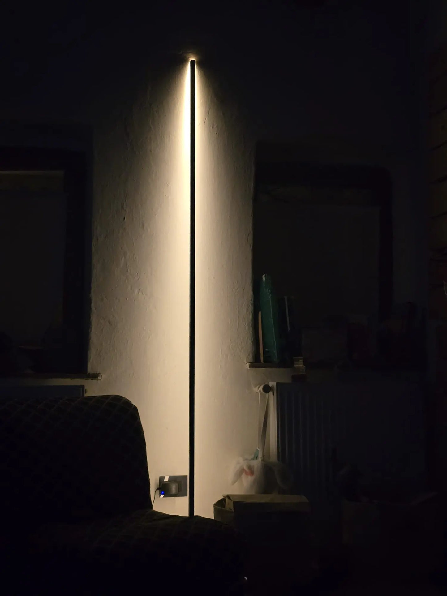 A refined interior with a sculptural floor lamp casting warm indirect light against a wall, creating soft shadows and a quiet luxury atmosphere.