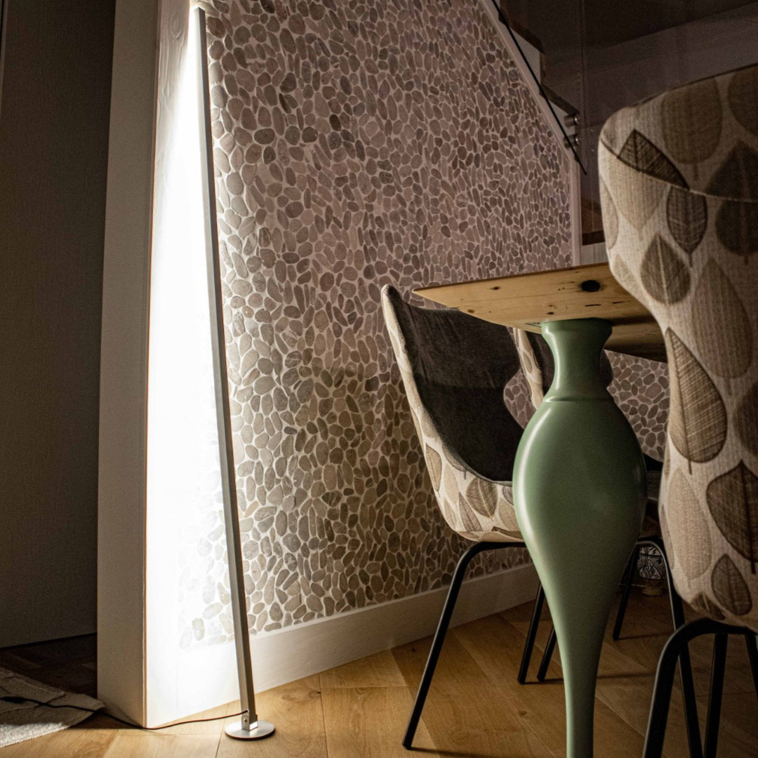minimalist sculptural floor lamp casting warm indirect light and soft shadows on a wall in a modern interior
