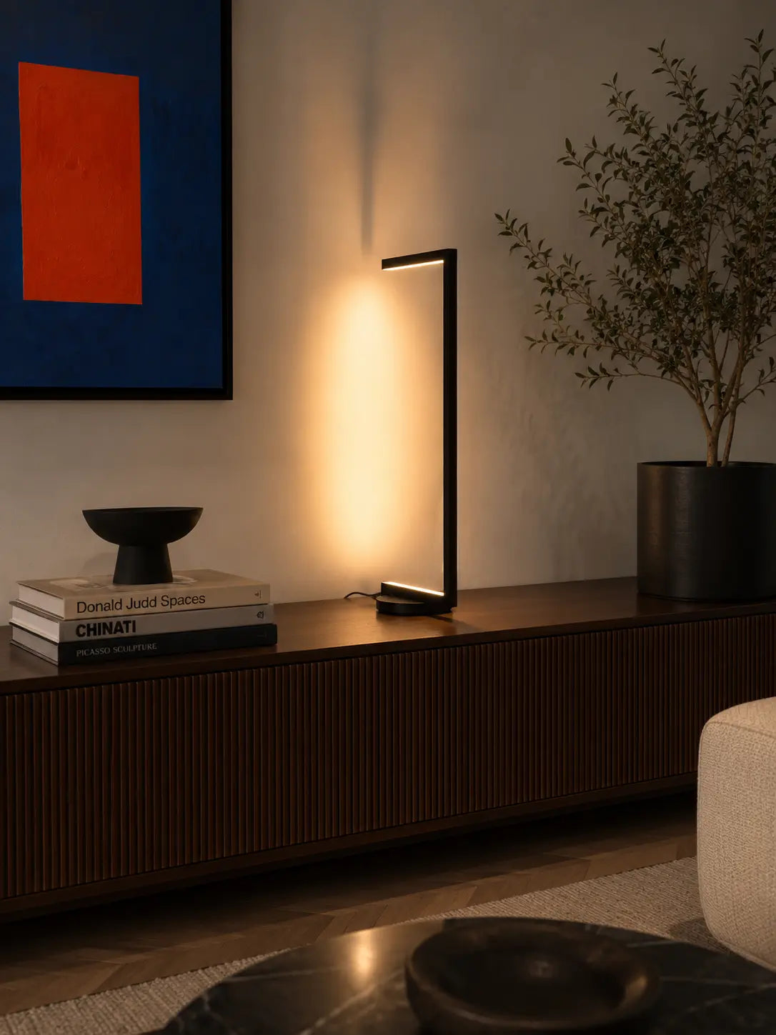 Tratto Table Lamp by Tommaso Cristofaro on a modern sideboard in a minimalist living room with colorful artwork and warm ambient light.