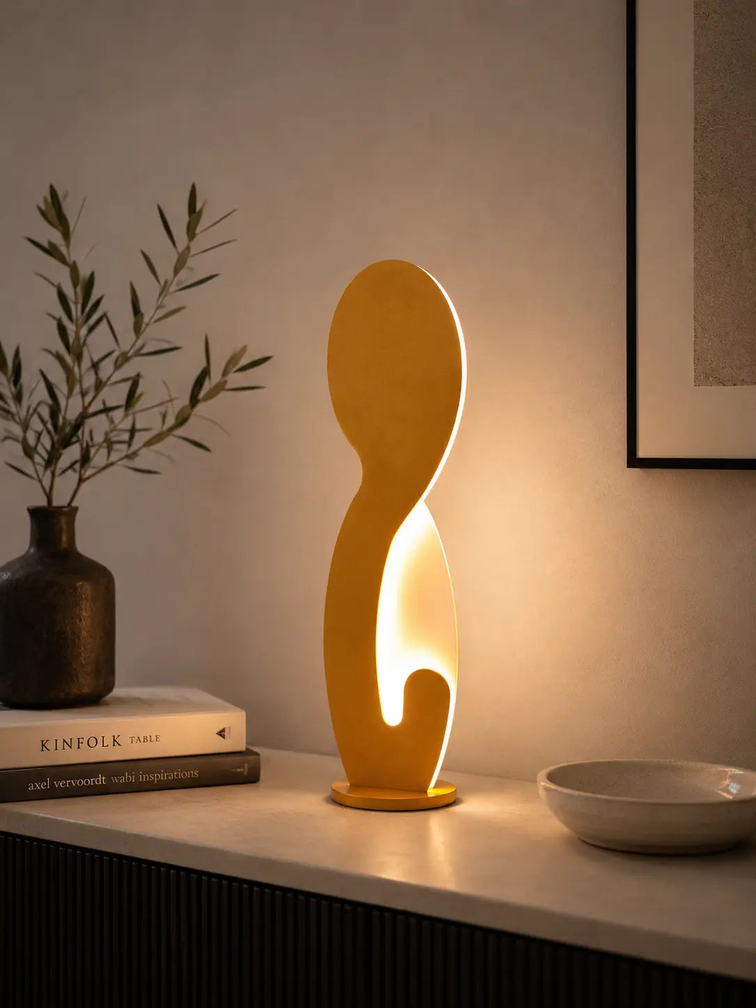 Yellow sculptural table lamp by Tommaso Cristofaro on a wooden sideboard in a minimalist living room, creating warm ambient light with elegant modern decor.