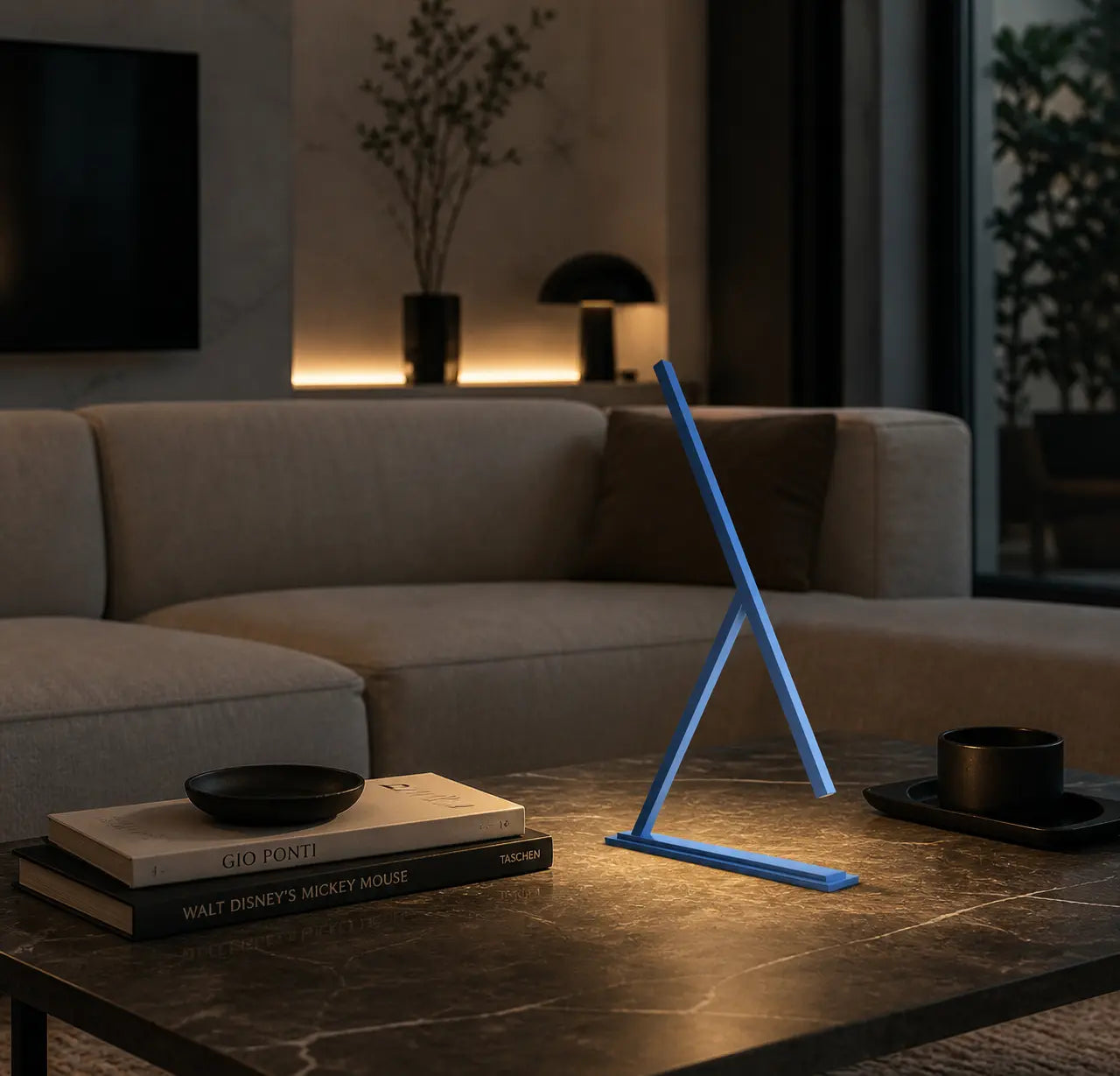 Achille table lamp in a modern living room, resting on a dark marble coffee table and casting a warm ambient glow beside design books and minimalist decor.